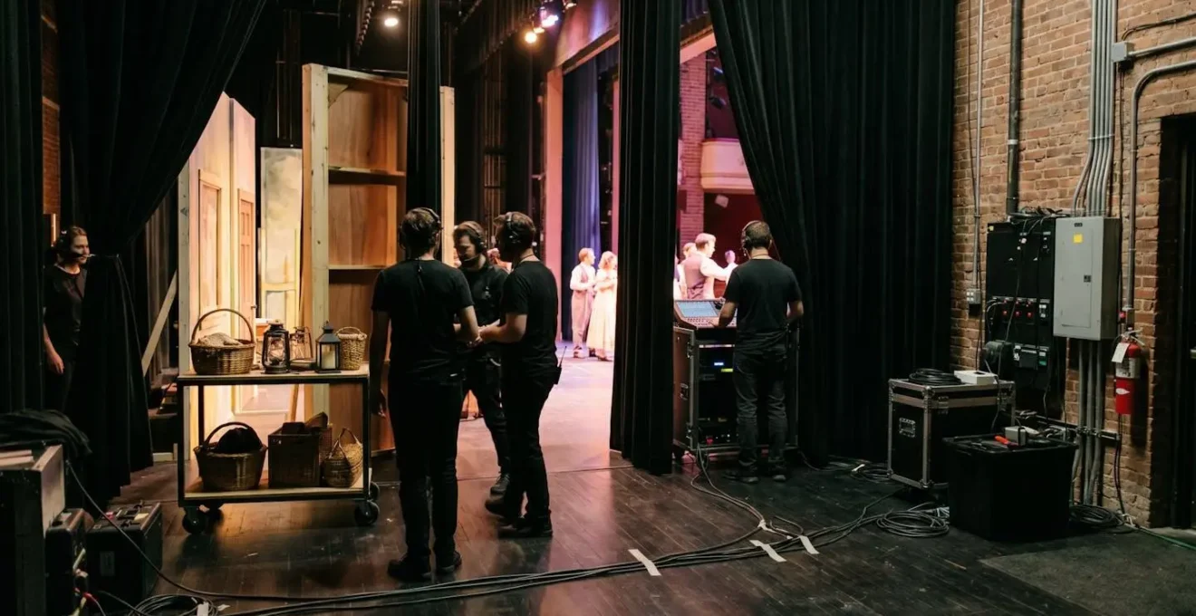 Vue depuis les coulisses d'une scène de théâtre avec éclairage tamisé et éléments de décor visibles